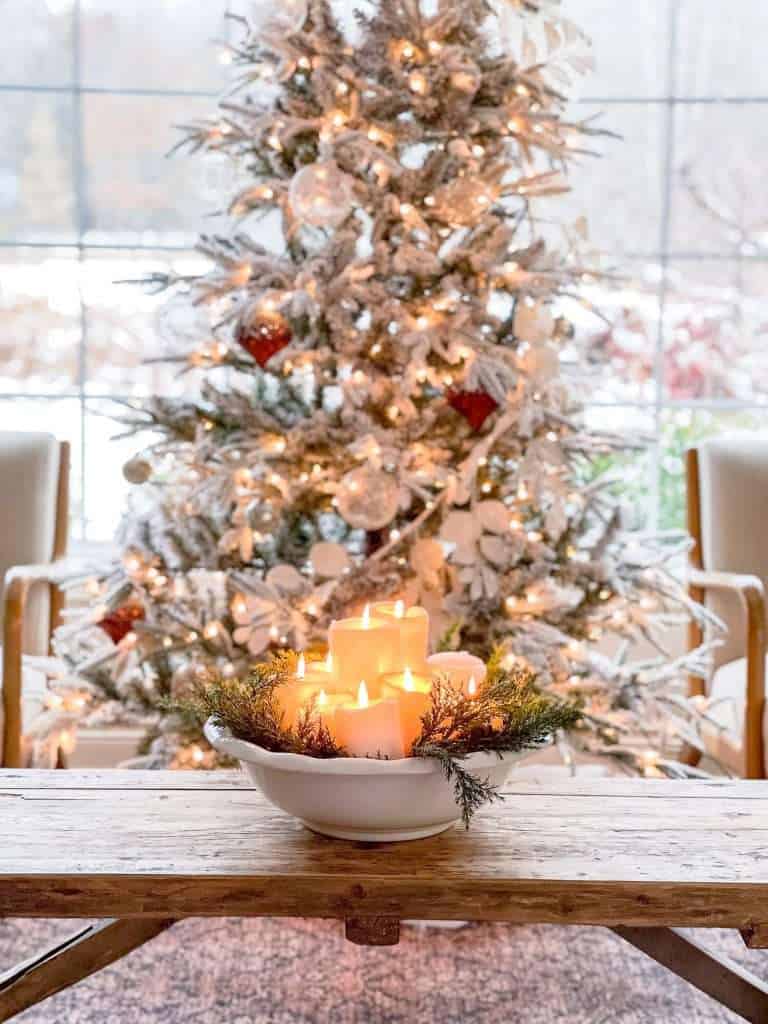 Candle centerpiece in front of a Christmas tree.