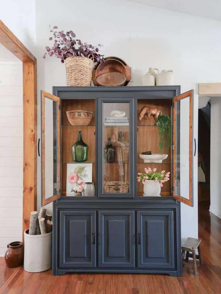 Black cabinet with farmhouse style decor on shelves.