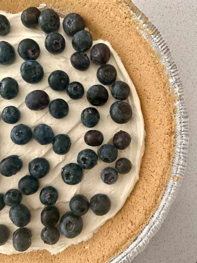 Blueberries being placed on no bake blueberry pie.
