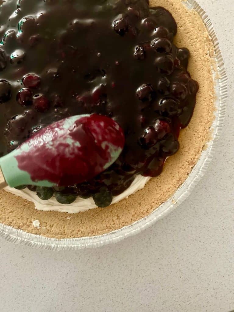 Placing blueberry topping into pie.