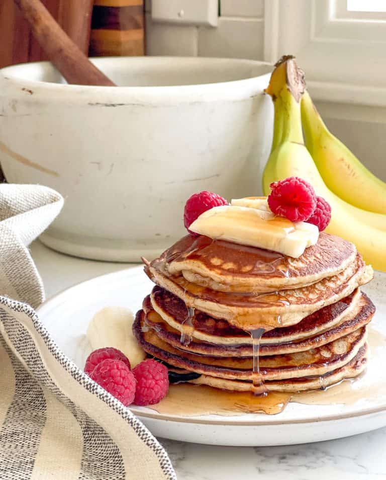 Stack of sourdough banana pancakes with fruit on top.