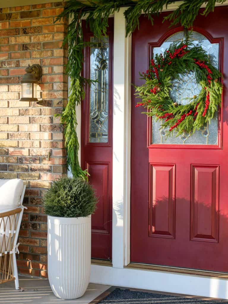 Red front door with evergreens.