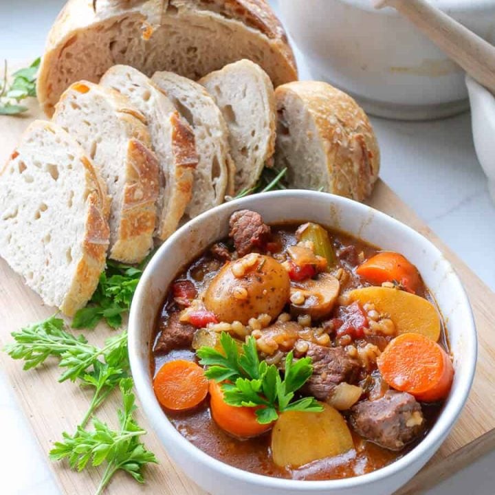 Bowl of beef barley stew on a counter with bread.