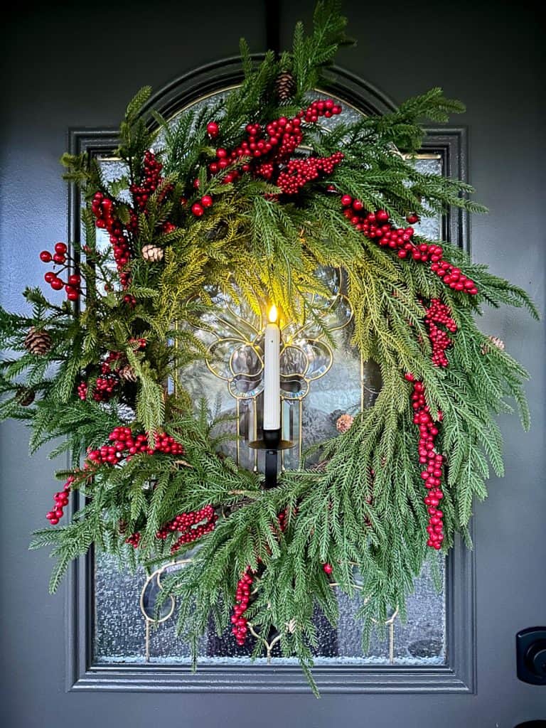 Red berry wreath hanging on the door with candle.