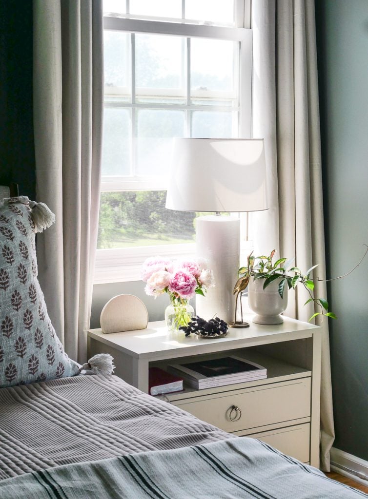 Nightstand in a bedroom with an alarm clock, potted plants, and a table lamp