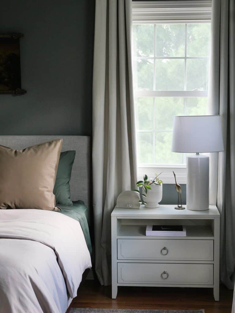 Nightstand in a bedroom with a potted plant and a table lamp on top
