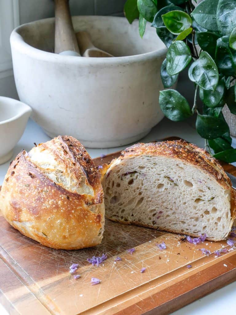Chive sourdough bread cut in half on a cutting board.