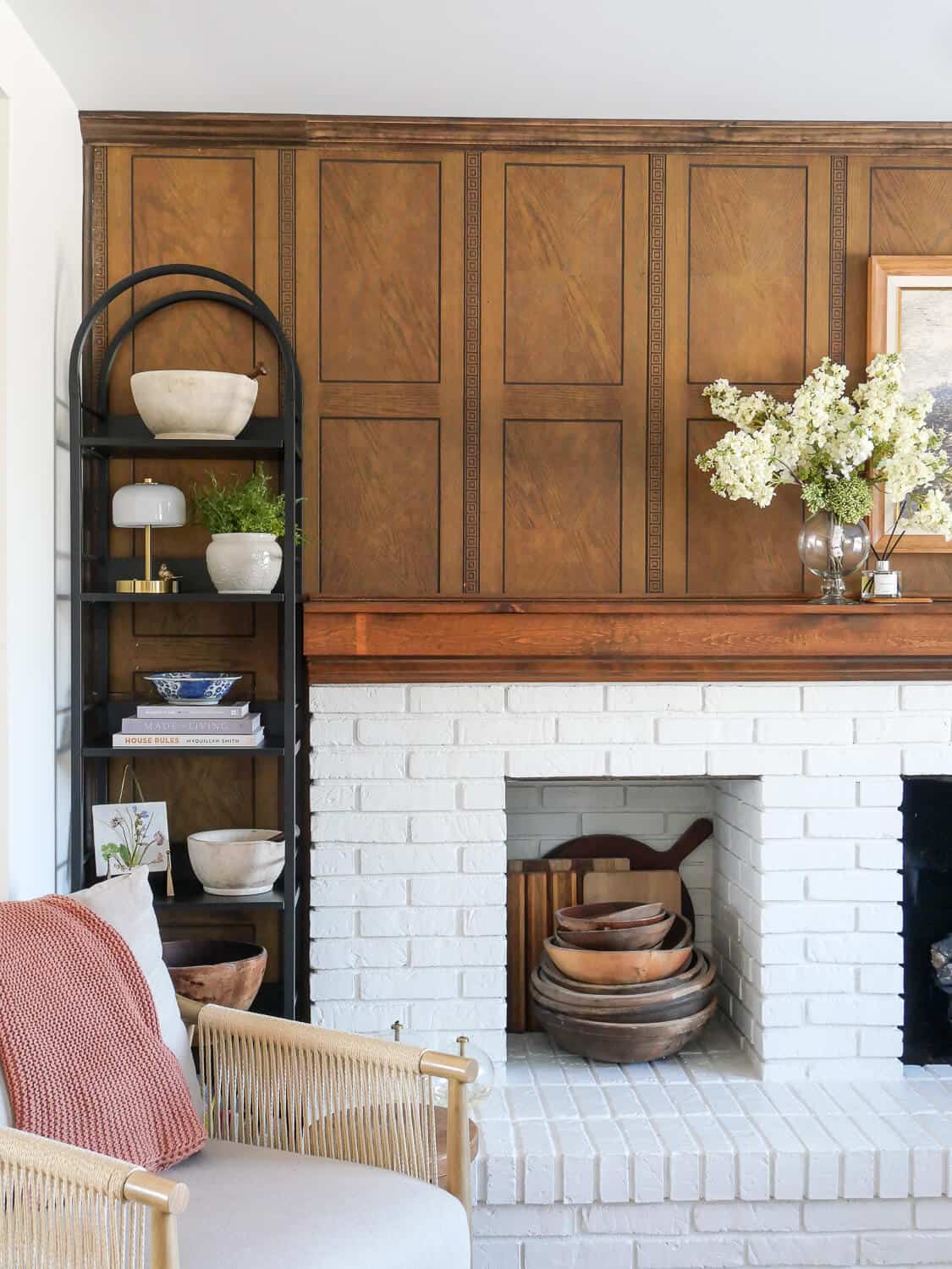 Open shelving styled with spring decor against walnut paneling next to a brick fireplace.