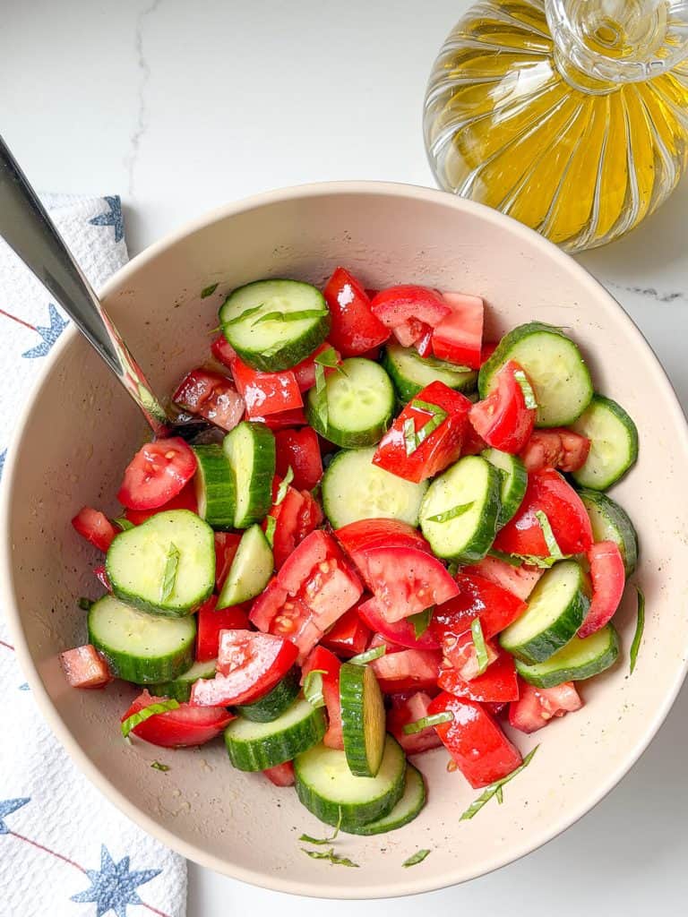 Cut up marinated tomatoes and cucumbers in a bowl.
